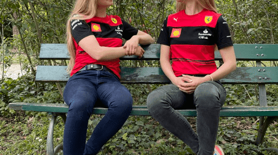 Blonde twins in sunglasses and Ferrari shirts chatting while seated on a bench